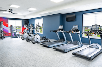 Gym with cardio equipment and weights in a room with windows
